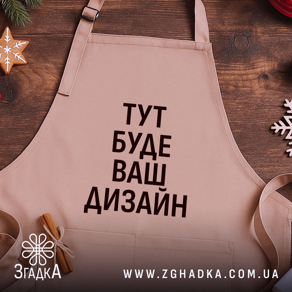 Фартух з вашим дизайном, бежевого кольору, зображений з верхнього ракурсу на дерев'яному фоні, навколо декор з новорічними елементами, принт чорного кольору з текстом 'ТУТ БУДЕ ВАШ ДИЗАЙН'.