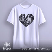 Футболка 100% любові всередині, біла, підвішена на вішалці, ракурс спереду, фон світло-сірий, принт у формі серця чорного кольору з написом "100% любові всередині" в декоративному шрифті.