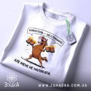 Футболка алкоголь це страшно, біла футболка, що лежить на поверхні, з принтом коня, який тримає пивні кухлі, фон світло-фіолетовий, текст на футболці: 'Алкоголь — це страшно. Але мене не налякати.', на футболці є етикетка.