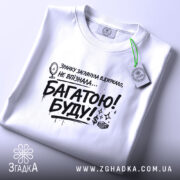Футболка багатою буду, білого кольору, розкладена на поверхні, фон світло-сірий, принт чорного кольору з текстом та малюнком дзеркала, присутня етикетка з зеленим шнурком.