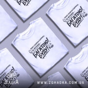 Футболка багатою буду, білого кольору, зображена на моделі з легким ракурсом спереду, фон світло-фіолетовий, принт чорного кольору з текстом та малюнком дзеркала.