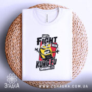 Футболка Бій з кунг-фу, біла, на столі, з верхнього ракурсу, фон світло-фіолетовий, принт з жовтим персонажем у чорному одязі, текстом 'LET'S FIGHT WITH KUNGFU SOUNDS!!!' на червоному фоні, на плетеній основі.