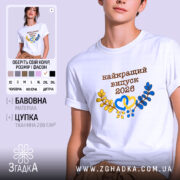 Футболка біла випуск 2026, на моделі, з коротким рукавом, фон світло-сірий, принт з написом 'найкращий випуск 2026' у коричневому кольорі, з жовтими та блакитними елементами у вигляді сердець і гілок.