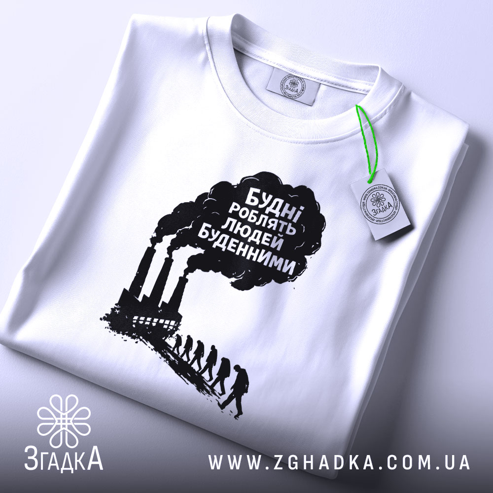 Футболка будні роблять людей буденними. Біла футболка, складена на поверхні, фон світло-сірий. Принт чорного кольору з текстом та зображенням димарів і силуетів людей, що йдуть, з зеленим ярликом.