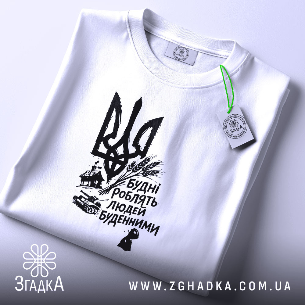 Футболка будні роблять людей буденними. Біла футболка, зображена на плоскій поверхні, фон світло-сірий. Принт чорного кольору з тризубом та написом 'Будні роблять людей буденними'. На футболці видно етикетку з зеленим шнурком.