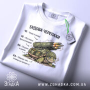 Футболка будова черепахи, біла, зображена зверху, фон світло-сірий, принт з черепахою та ракетною установкою, текст на українській мові, на комірці видна етикетка.
