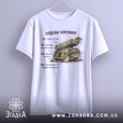 Футболка будова черепахи, біла, підвішена на вішалці, фон світло-сірий, принт з черепахою та ракетною установкою, текст на українській мові, видно деталі принта.