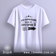 Футболка був нормальний поки не зустрів її, біла футболка, підвішена на вішалці, фон світло-сірий, принт чорного кольору з текстом та стрілкою.