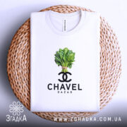 Футболка Chavel Bazar білого кольору, складена на кошику, ракурс зверху, фон світло-фіолетовий, принт з зображенням пучка шпинату та логотипом CHAVEL BAZAR під ним.