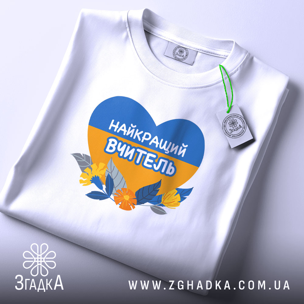 Футболка для вчителя випускників, біла, на плоскій поверхні, з принтом у формі серця, що містить синій і жовтий кольори, з написом 'НАЙКРАЩИЙ ВЧИТЕЛЬ' та квітами, з етикеткою, що звисає з коміра.