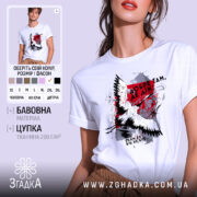 Футболка добре там де дім. Біла футболка на моделі, з принтом на грудях, що містить зображення птаха та текст. Фон світло-фіолетовий, модель позує з легким усмішкою, підкреслюючи стиль футболки.