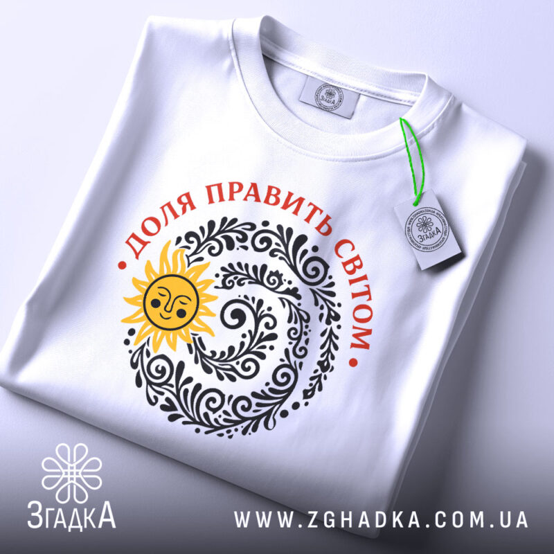 Футболка Доля править світом, біла, на плоскому фоні, з верхнього ракурсу, принт з сонцем та візерунками чорного кольору, текст червоним кольором, етикетка з зеленим шнурком.