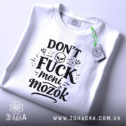 Футболка Don’t Fuck meni mozok, біла, складена на поверхні, ракурс зверху, фон світло-сірий, принт чорного кольору з черепом та декоративними елементами, на ярлику зелена стрічка.