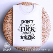 Футболка Don’t Fuck meni mozok, біла, складена на плетеній кошику, ракурс зверху, фон світло-сірий, принт чорного кольору з черепом та декоративними елементами.