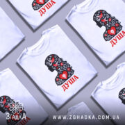 Футболка Душа український стиль, біла, зображена на моделі з легким ракурсом, фон світло-фіолетовий, принт з силуетом жінки, прикрашеним червоними пташками та квітами, текст 'ДУША' червоним кольором.