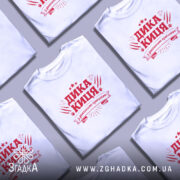 Футболка дика киця білого кольору, зображена на моделі з коротким рукавом, фон світло-фіолетовий, принт червоного кольору з написом 'ДИКА КИЦЯ' та декоративними елементами.