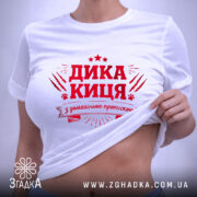 Футболка дика киця білого кольору, складена на поверхні, фон світло-сірий, принт червоного кольору з написом 'ДИКА КИЦЯ' та декоративними елементами, видима етикетка.