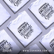 Футболка експерт з перегляду серіалів, біла, на моделі, з легким макіяжем, фон світло-фіолетовий, принт чорного кольору з текстом 'Головний експерт з перегляду серіалів' та декоративними елементами.