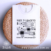 Футболка електрична схема, біла, складена на плоскій поверхні, фон світло-сірий, принт з чорними елементами електронної схеми та текстом на українській мові, розташована на плетеній основі.