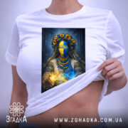 Футболка етно мотанка, біла, на плоскій поверхні, з принтом жінки в українському національному вбранні, фон світло-сірий, деталі принта включають жовті соняшники та синю маску, прикріплена етикетка з логотипом.