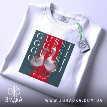Футболка GUSSI з гусьми, біла, складена на поверхні, ракурс зверху, фон світло-сірий, принт з двома гусьми на червоному та зеленому фоні з написами GUSSI.