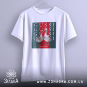 Футболка GUSSI з гусьми, біла, підвішена на вішалці, ракурс спереду, фон світло-сірий, принт з двома гусьми на червоному та зеленому фоні з написами GUSSI.