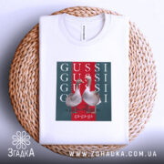 Футболка GUSSI з гусьми, біла, складена на кошику, ракурс зверху, фон світло-сірий, принт з двома гусьми на червоному та зеленому фоні з написами GUSSI.