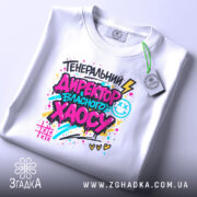 Футболка генеральний директор хаосу, біла, на столі, фон світло-сірий, принт кольоровий з написом 'ГЕНЕРАЛЬНИЙ ДИРЕКТОР ВЛАСНОГО ХАОСУ', деталі принта чіткі, етикетка на комірці.