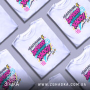 Футболка генеральний директор хаосу, біла, на моделі, фон світло-фіолетовий, принт кольоровий з написом 'ГЕНЕРАЛЬНИЙ ДИРЕКТОР ВЛАСНОГО ХАОСУ', яскраві кольори, графічні елементи, смайлик, блискавка.