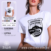 Футболка гірська свобода, біла, на моделі, з легким ракурсом спереду, фон світло-фіолетовий, принт чорного кольору з написом 'НАРОДЖЕНИЙ БУТИ ДИКИМ' та зображенням гір і дороги.