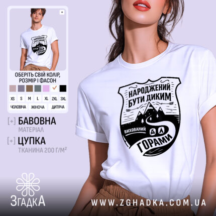 Футболка гірська свобода, біла, на моделі, з легким ракурсом спереду, фон світло-фіолетовий, принт чорного кольору з написом 'НАРОДЖЕНИЙ БУТИ ДИКИМ' та зображенням гір і дороги.