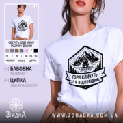 Футболка гори кличуть, біла, на моделі, з легким макіяжем, фон світло-фіолетовий, принт з горами, вогнищем і написом 'Гори кличуть! Я відповідаю.'