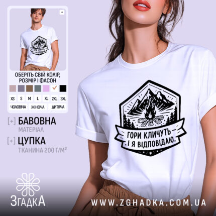 Футболка гори кличуть, біла, на моделі, з легким макіяжем, фон світло-фіолетовий, принт з горами, вогнищем і написом 'Гори кличуть! Я відповідаю.'