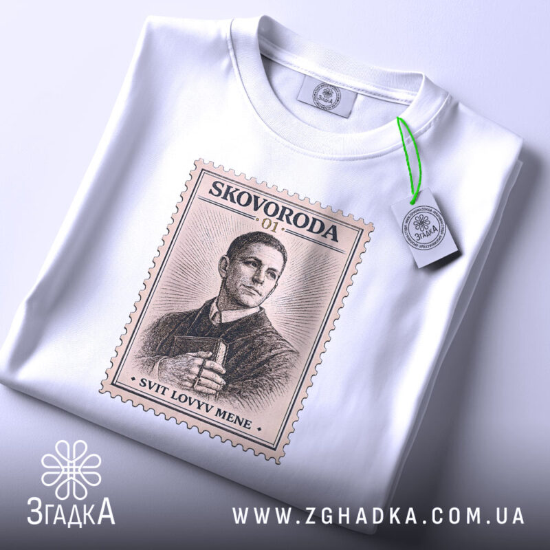 Футболка Григорій Сковорода, біла, зображена на столі, ракурс зверху, фон світло-сірий, принт у вигляді поштової марки з портретом Григорія Сковороди та написом 'SVIT LOVYV MENE', на футболці є етикетка.