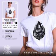 Футболка я дівчина вогонь, біла, на моделі, з принтом у вигляді вогню та написом "Я Дивчина Вогонь", фон світло-фіолетовий, деталі принта чорні та декоративні.