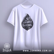 Футболка я дівчина вогонь, біла, підвішена на вішалці, з принтом у вигляді вогню та написом "Я Дивчина Вогонь", фон світло-сірий, деталі принта чорні.