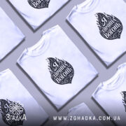 Футболка я дівчина вогонь, біла, на моделі, з принтом у вигляді вогню та написом "Я Дивчина Вогонь", фон світло-фіолетовий, деталі принта чорні та декоративні.