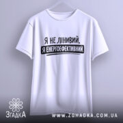 Футболка я енергоефективний, біла, підвішена на вішалці, ракурс спереду, фон світло-сірий, принт чорного кольору з текстом 'Я не лінивий, я енергоефективний'.