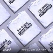 Футболка я енергоефективний, біла, зображена на чоловікові, ракурс спереду, фон світло-фіолетовий, принт чорного кольору з текстом 'Я не лінивий, я енергоефективний'.