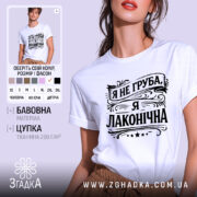 Футболка я не груба. Біла футболка з коротким рукавом, зображена з ракурсу спереду, на фоні світло-фіолетового кольору. Принт чорного кольору з написом "Я не груба, я лаконічна" в стилі декоративного шрифту, розташований по центру.