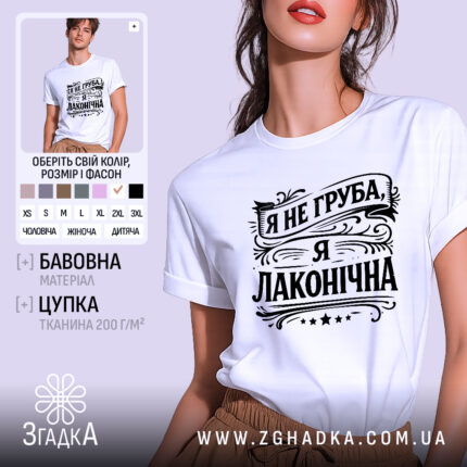 Футболка я не груба. Біла футболка з коротким рукавом, зображена з ракурсу спереду, на фоні світло-фіолетового кольору. Принт чорного кольору з написом "Я не груба, я лаконічна" в стилі декоративного шрифту, розташований по центру.