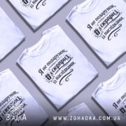 Футболка я не подарунок, біла футболка на чоловікові, з коротким рукавом, на фоні світло-сірого кольору, принт чорного кольору з текстом "Я не подарунок, я сюрприз із наслідками" та зображенням подарунка.