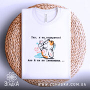 Футболка Я не подарунок. Біла футболка, складена на плетеній кошику, фон білий. Принт з ведмедиком, який тримає кульки, з написом українською мовою, видна етикетка.
