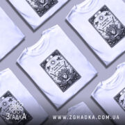 Футболка Я в серці має білий колір, зображена на моделі, що позує з легким усмішкою. Принт на футболці чорного кольору з елементами графіки, що включає серце, квіти та мечі, розташований по центру. Фон світло-фіолетовий, що підкреслює яскравість дизайну.