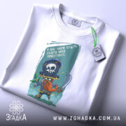 Футболка я вас навчу: біла футболка, на якій зображений той же принт пірата, розкладена на поверхні, фон світло-сірий, видно етикетку з зеленим шнурком.