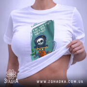 Футболка я вас навчу: біла футболка, на якій зображений той же принт пірата, розкладена на поверхні, фон світло-сірий, видно етикетку з зеленим шнурком.
