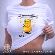 Футболка я важка людина. Біла футболка, складена на поверхні, з принтом жовтого злитка золота. Принт має яскраві кольори, текст зверху: 'Так, я важка людина!' Фон світлий, акцент на футболці.