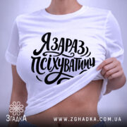 Футболка я зараз псіхуватиму, біла, на плоскій поверхні, фон світлий, принт чорний, з написом 'Я ЗАРАЗ, ПСІХУВАТИМУ' у стилі рукописного шрифту, з етикеткою на комірці.