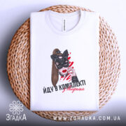 Футболка йду в комплекті з валідолом, біла, зображена на плоскій поверхні, фон світло-фіолетовий, принт з жінкою в масці кота, написом, розташована на плетеній основі.