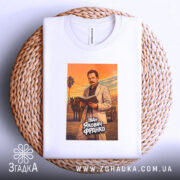 Футболка Іван Франко білого кольору, розкладена на плетеній кошику. Принт зображає чоловіка в світлому костюмі, який читає книгу, на фоні оранжевого заходу сонця. Кошик додає текстури до зображення, фон світлий.